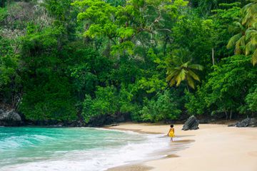 A woman in a yellow dress walks along the Playa Colorada beach in the Dominican Republic