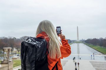 A mature woman taking a photo of Washington Monument across pond at National Mall 