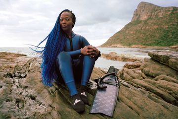 Portrait of free diver Zandile Ndhvolu in a wet suit sitting on rocks waterside in Cape Town